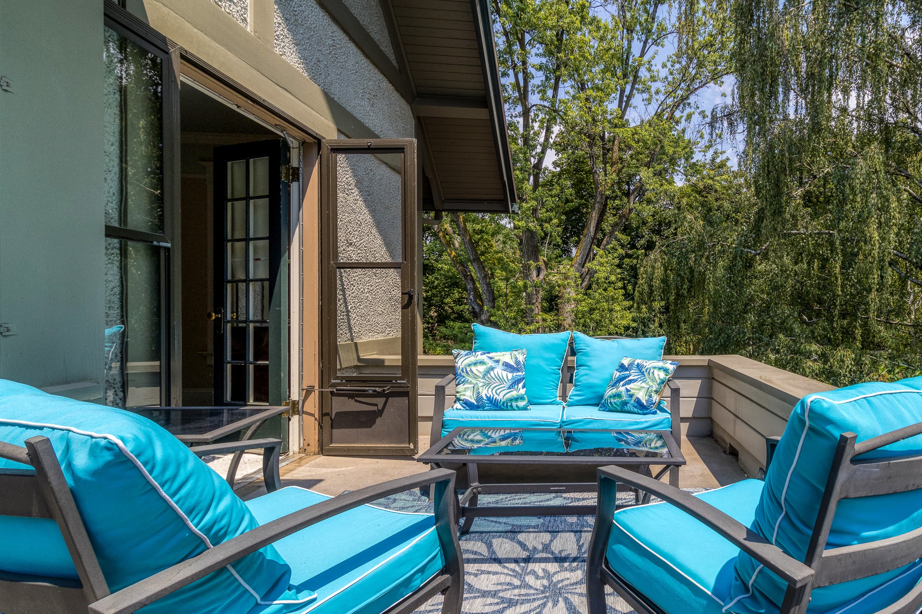 Private outdoor balcony with a set of two chairs & loveseat with bright blue cushions.