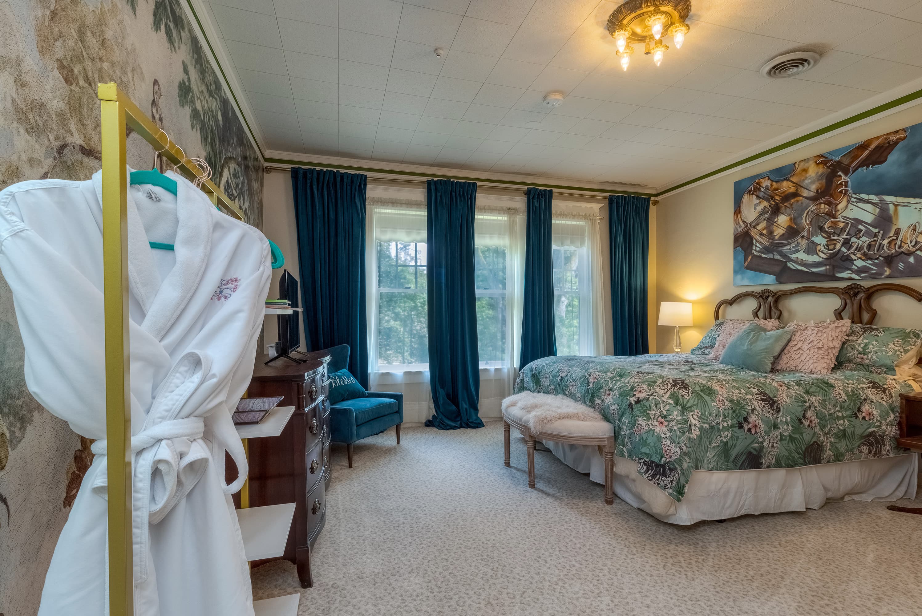 A luxurious and spacious bedroom with a king bed, elegant teal curtains, and bold artwork.