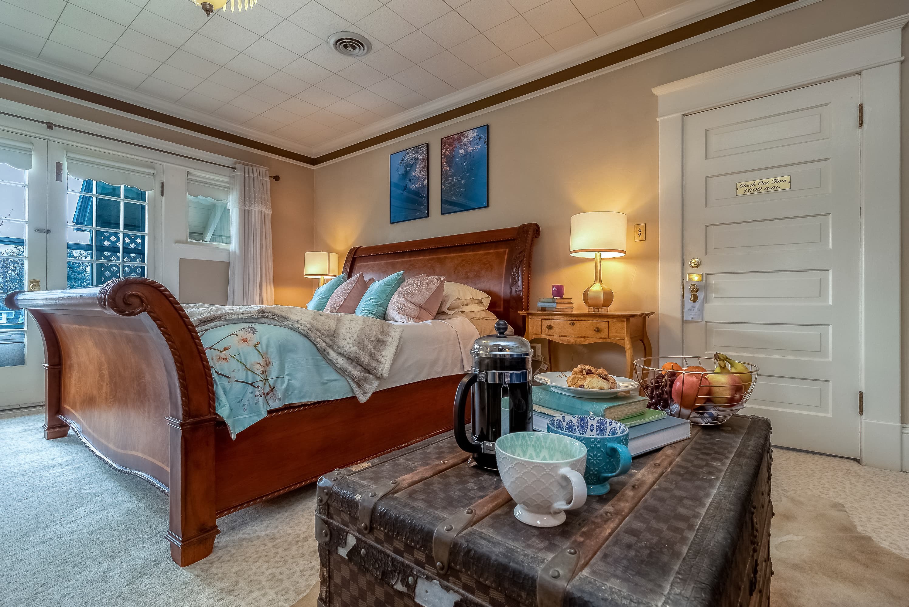 A inviting bedroom featuring a king-size wooden sleigh bed with colorful pillows, a vintage trunk serving as a coffee table, and soft lighting.