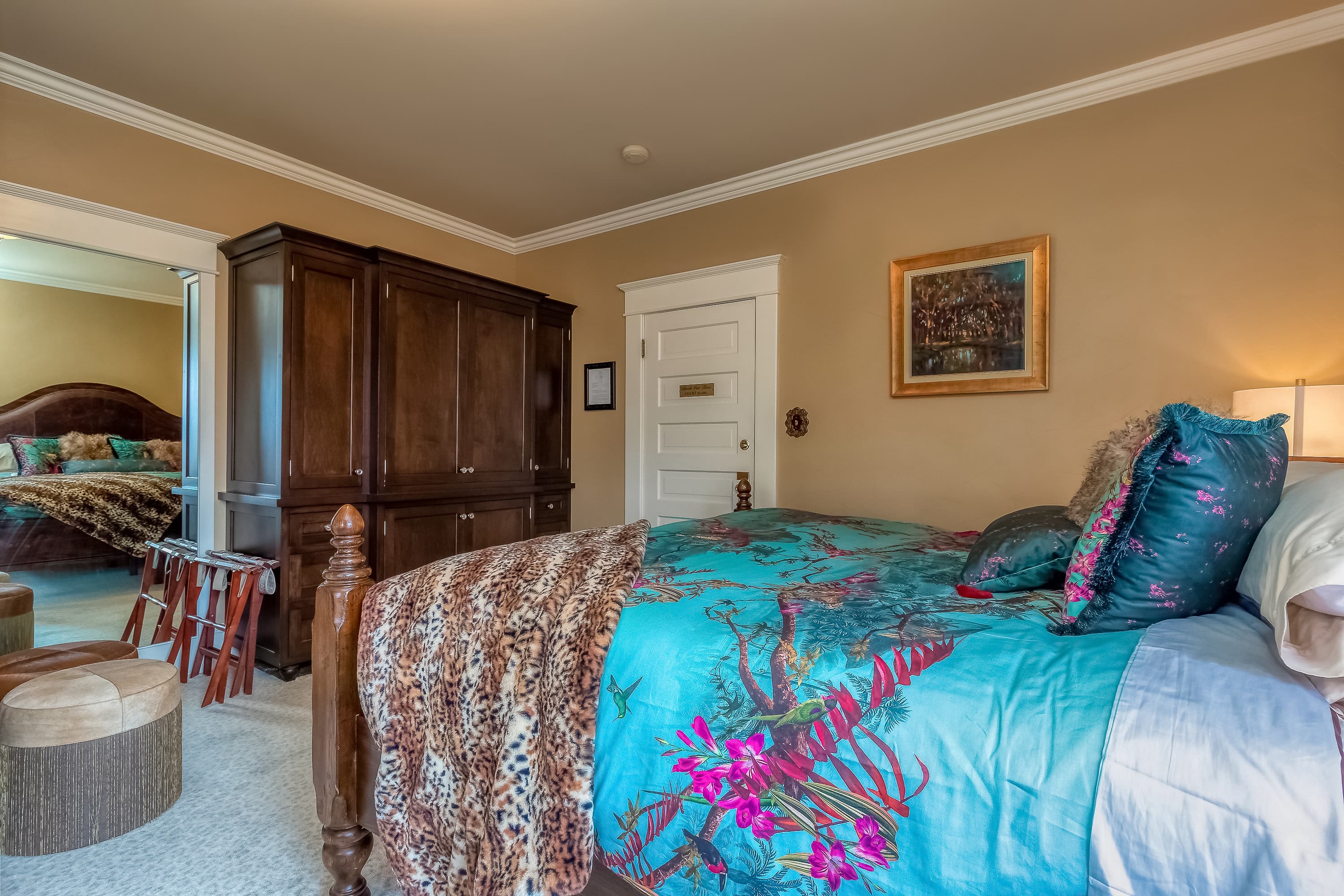 A richly decorated bedroom with a wooden king-size bed, vibrant bedding, and a large armoire.