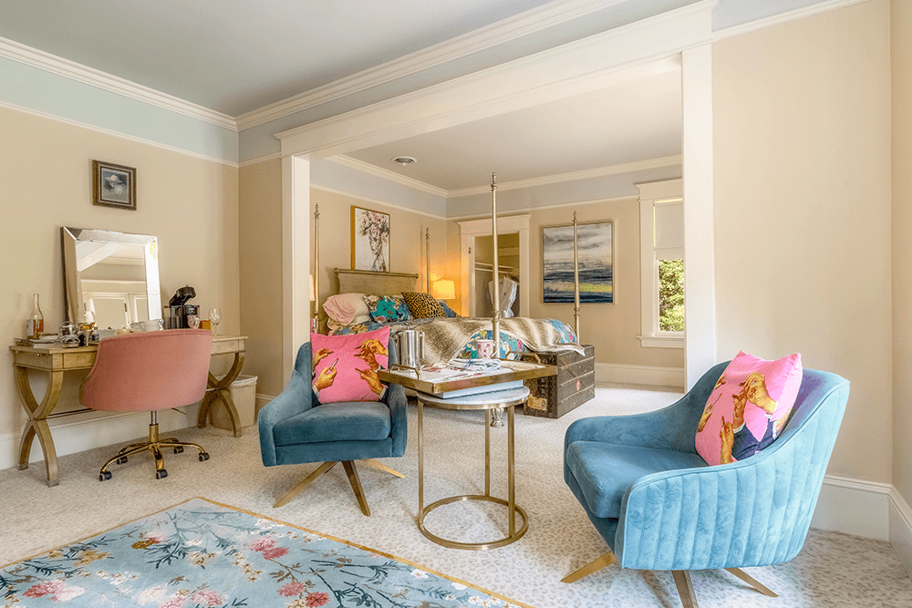 right and inviting bedroom sitting area with two teal chairs and pink chair stationed at a dressing table