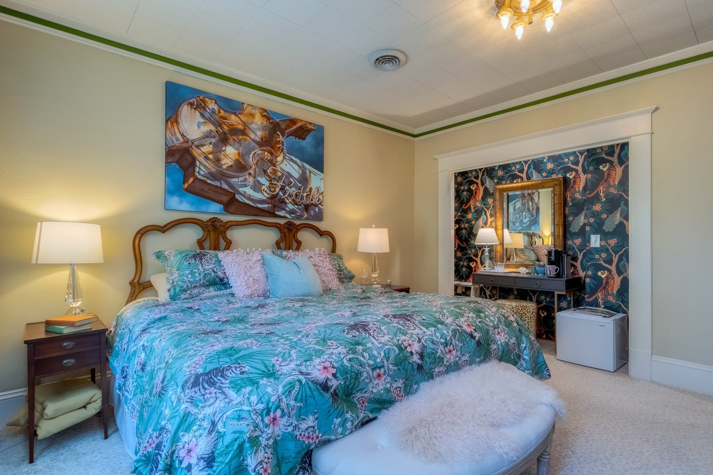 A cozy bedroom featuring a floral-patterned bedspread, vintage furniture, and a decorative wall with a mirror.