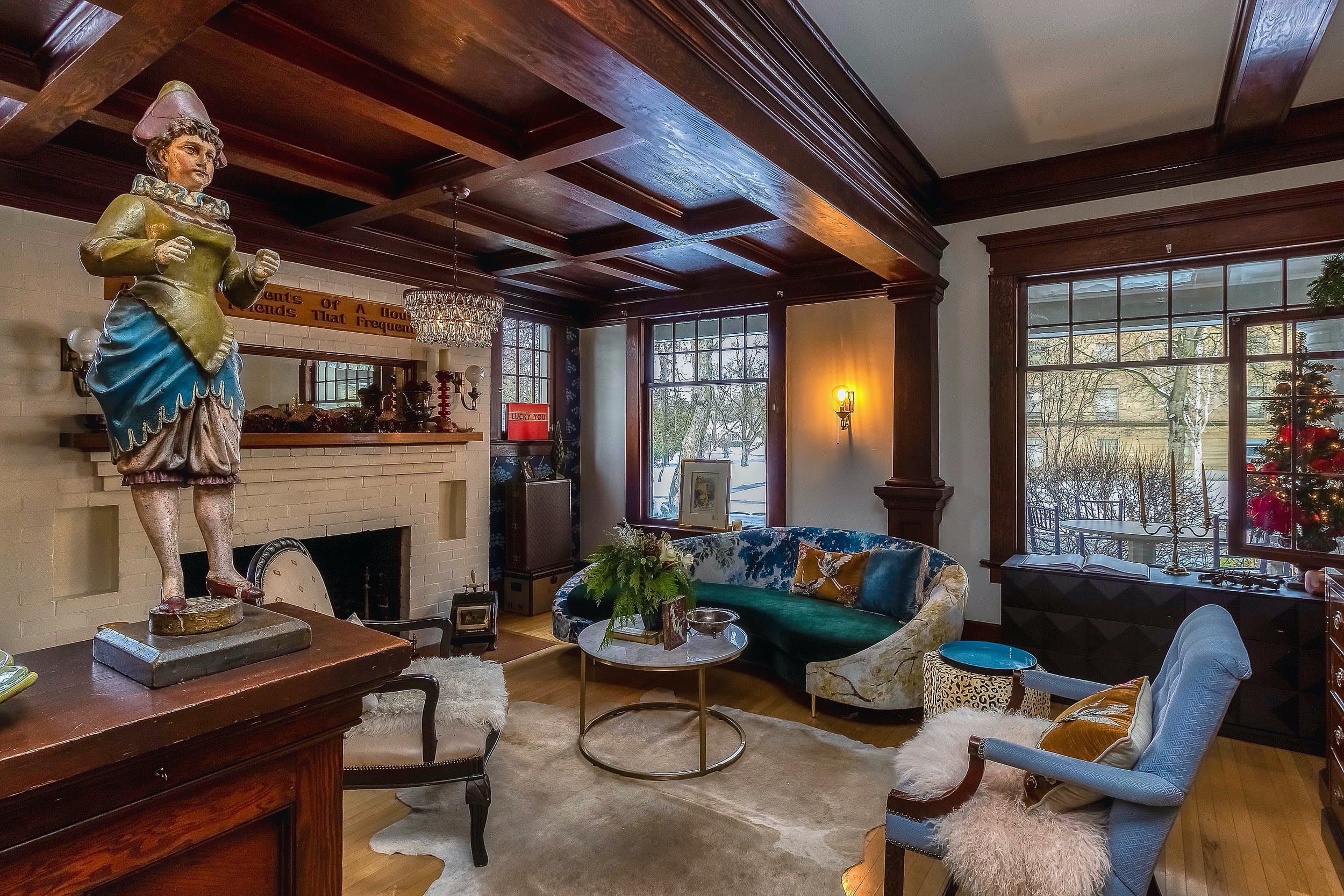 A cozy living room featuring a vintage statue, elegant furniture, and large windows with winter views.