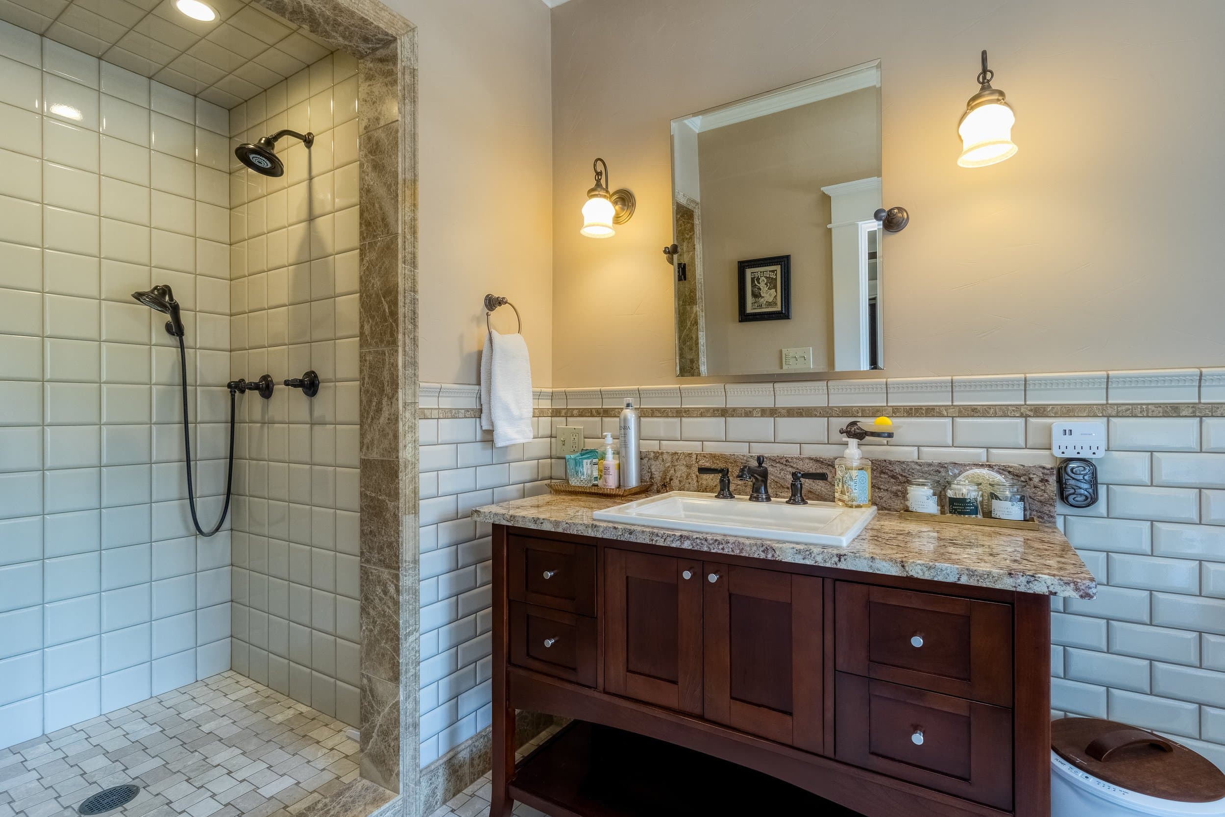 A modern bathroom featuring a walk-in shower, a granite countertop sink, and stylish lighting.