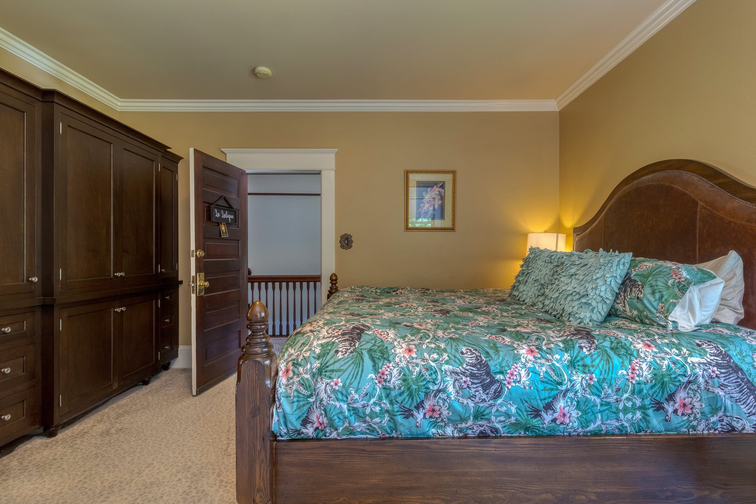 A cozy bedroom featuring a large bed with floral bedding, wooden furniture, and a doorway leading to a staircase.