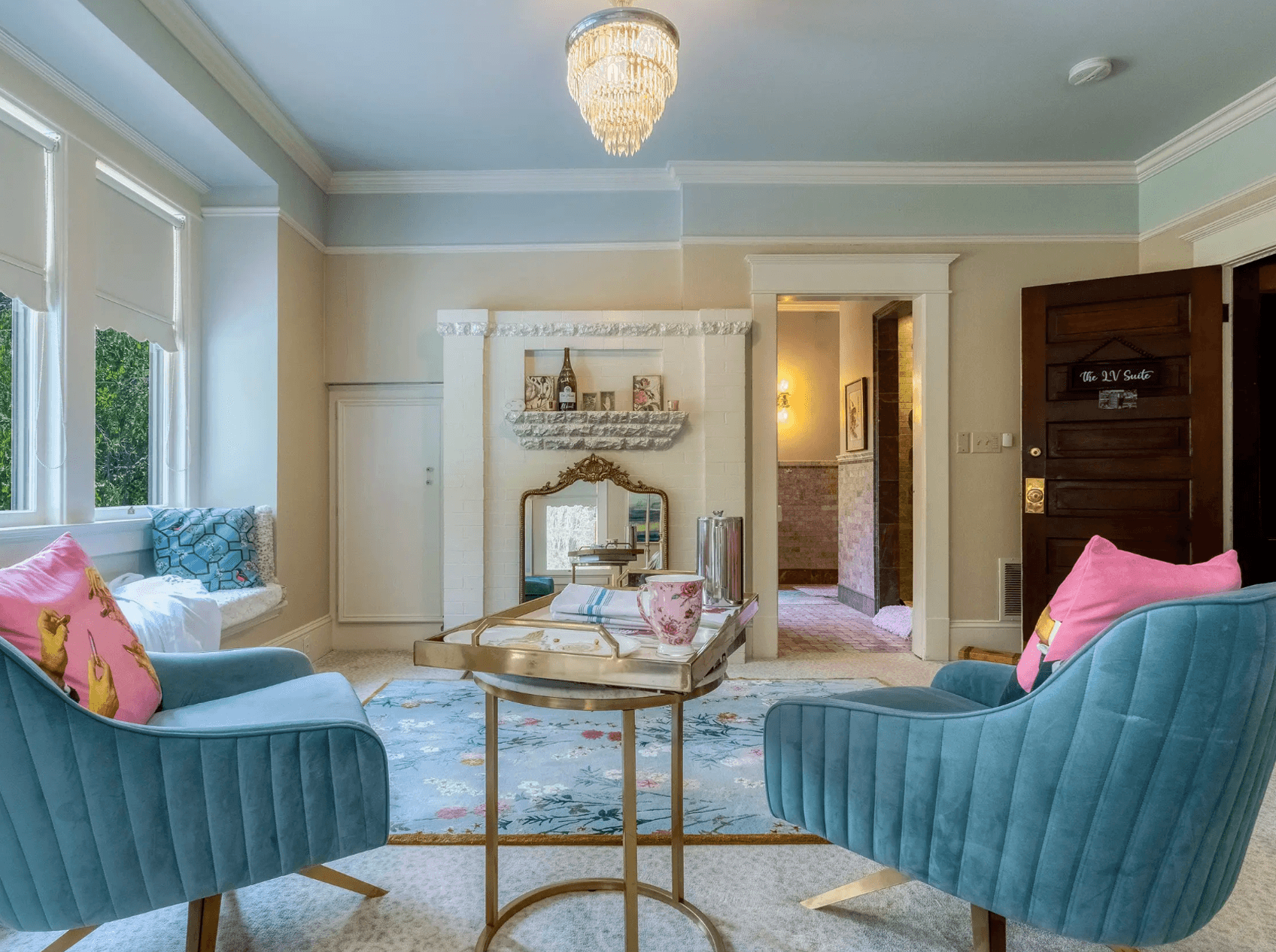 A bright, elegantly furnished living room featuring two teal chairs, a small coffee table, and decorative accents.