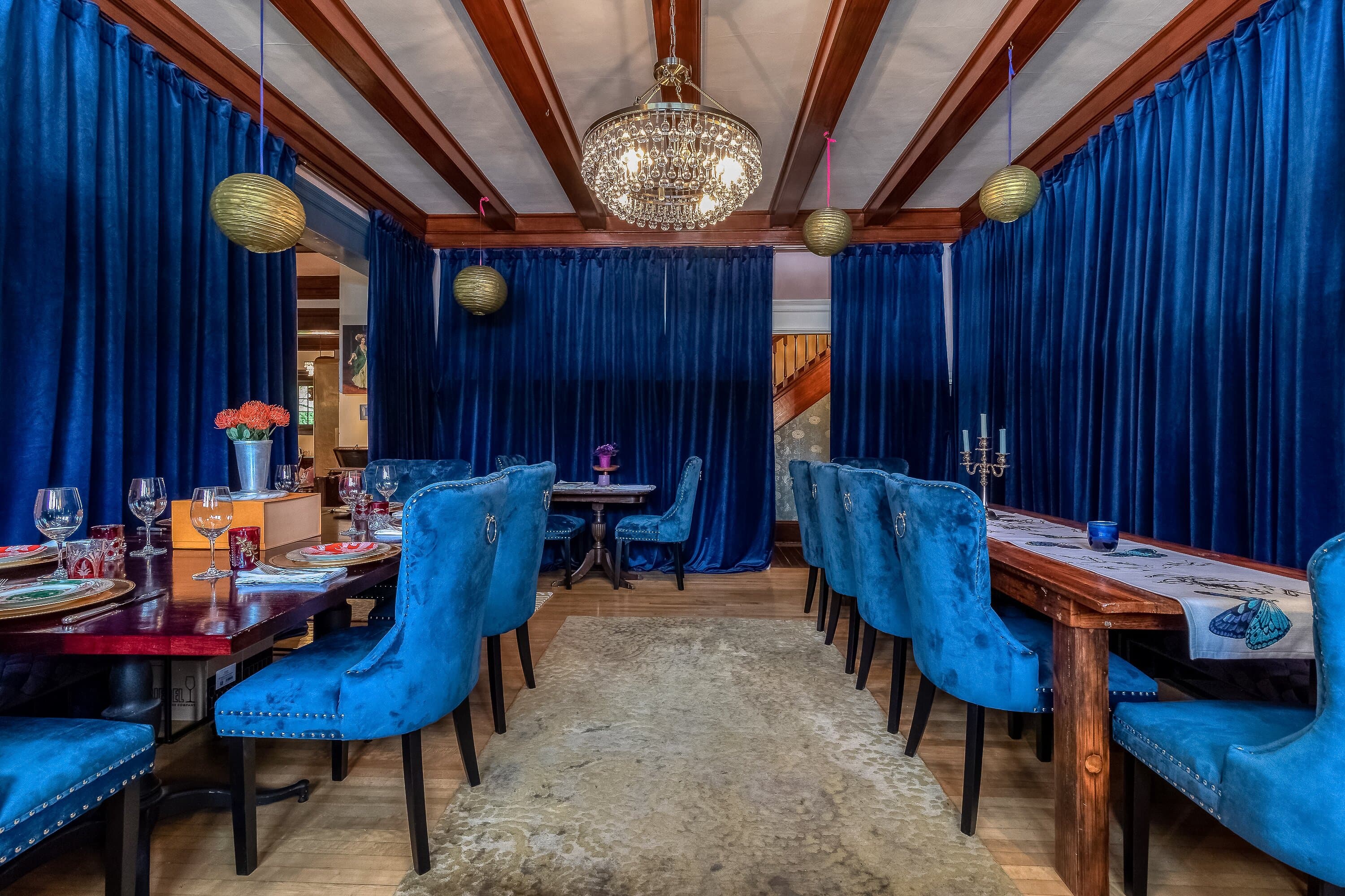 A cozy dining room with blue velvet curtains, plush chairs, and a sparkling chandelier.