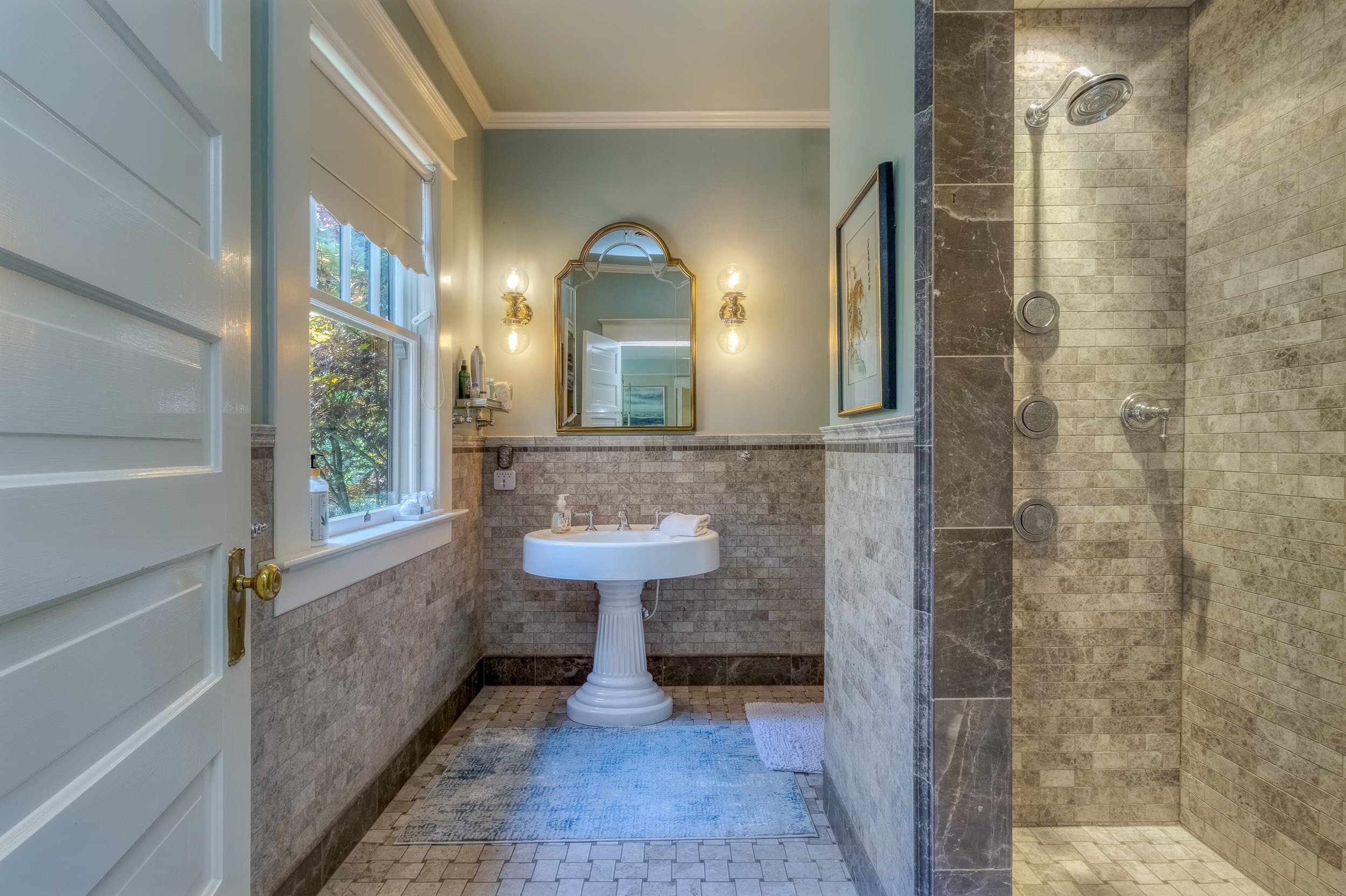 A stylish bathroom featuring a pedestal sink, a framed mirror, and a walk-in shower with modern fixtures.