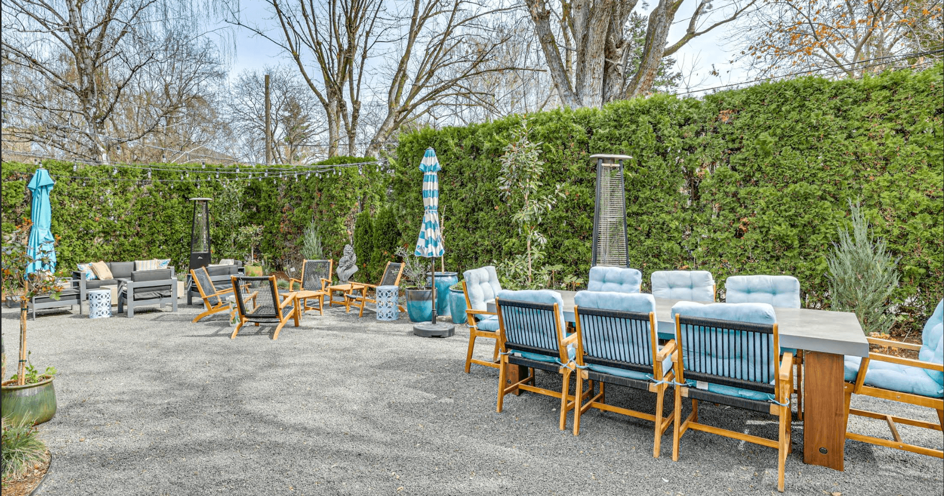 A cozy outdoor seating area surrounded by greenery, featuring wooden chairs, tables, and umbrellas.