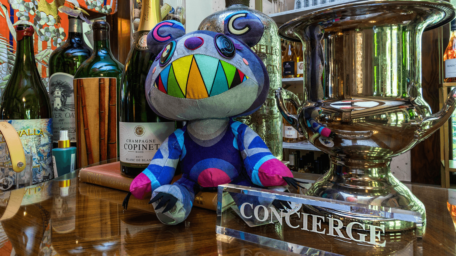 Stuffed toy sits on countertop next to wine bottles and acrylic sign that reads CONCIERGE