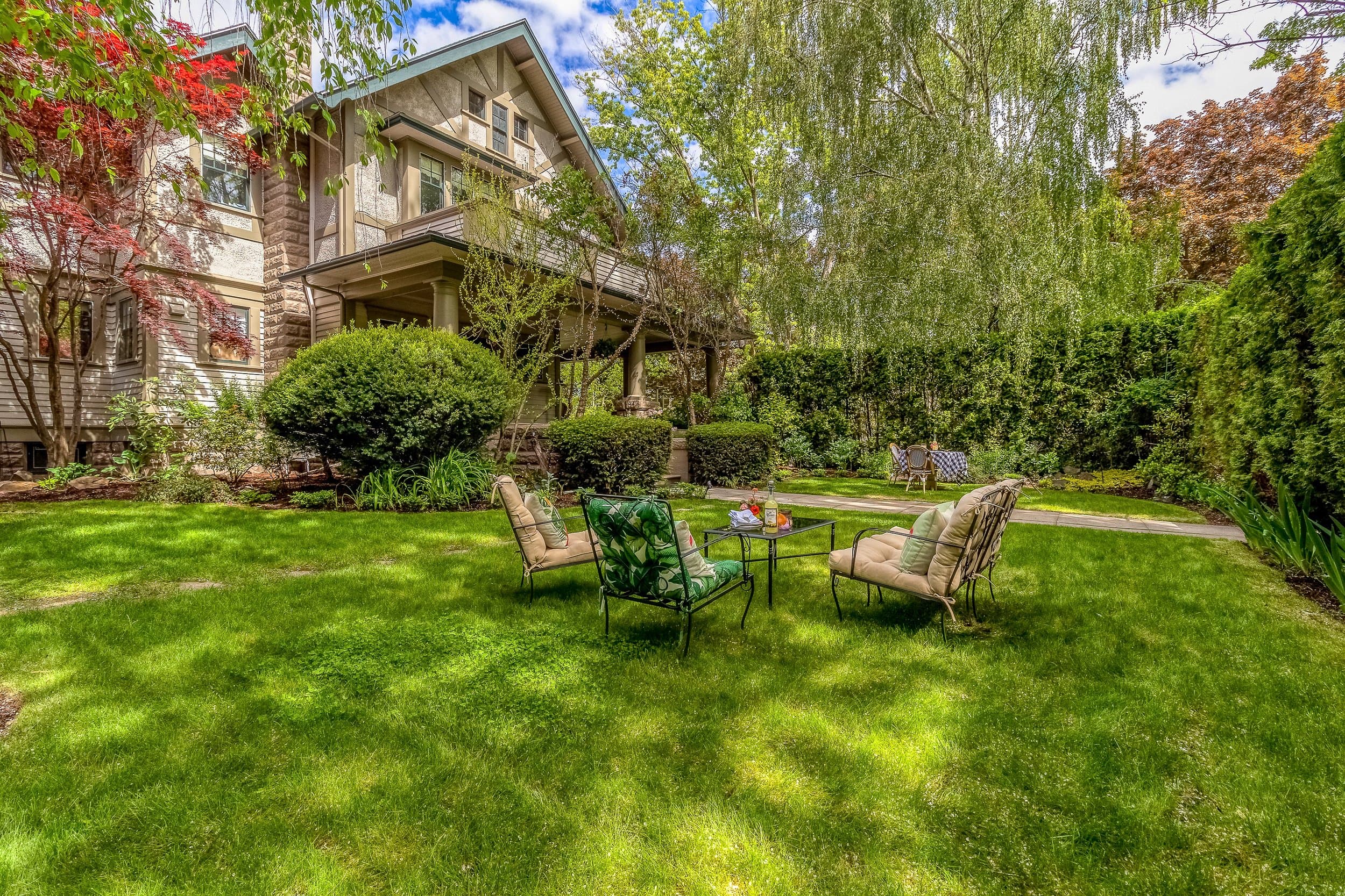 A cozy backyard with green grass, lounge chairs around a small table, and a charming house in the background.