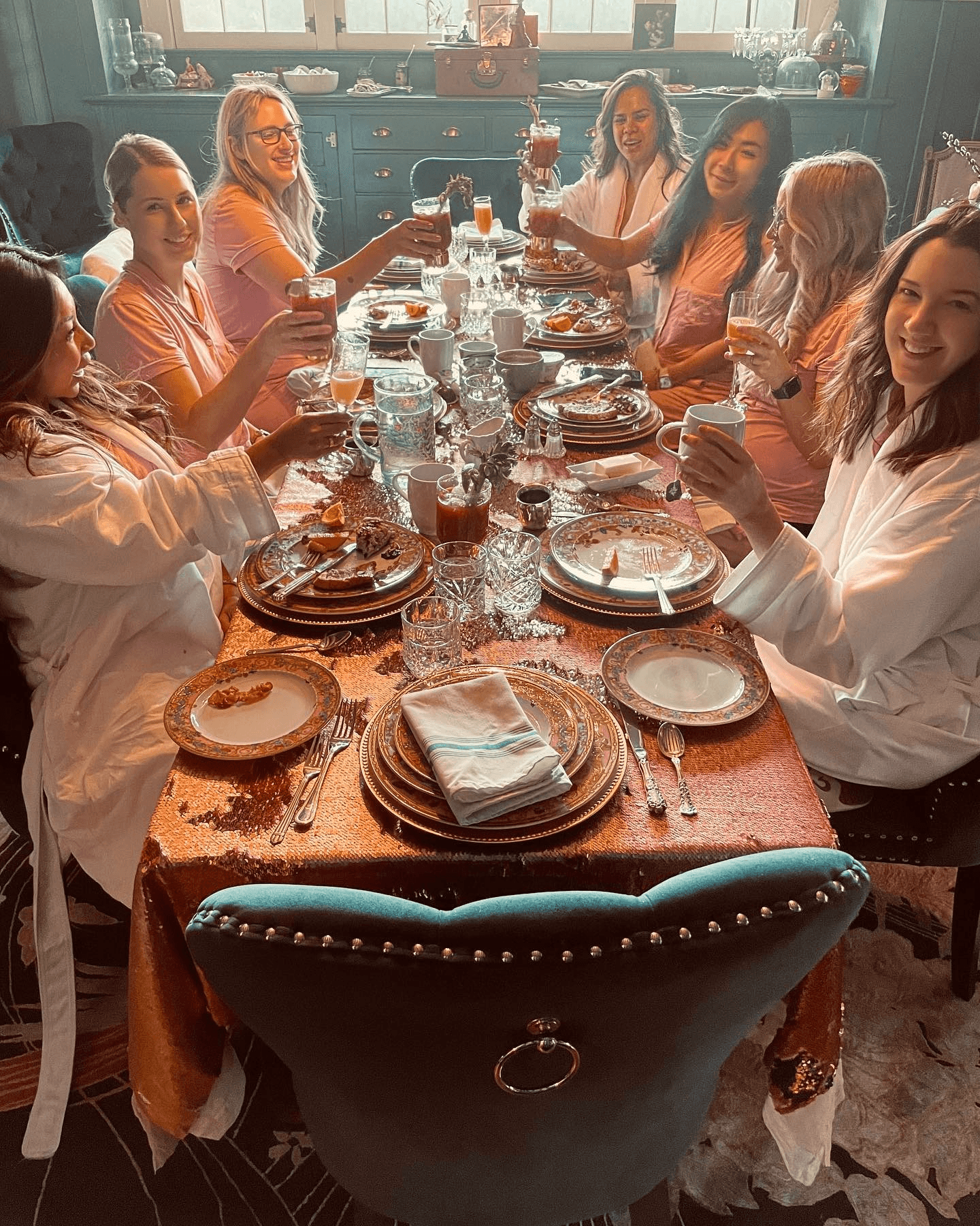 A group of eight women in pink attire toast with drinks at a beautifully set dinner table.