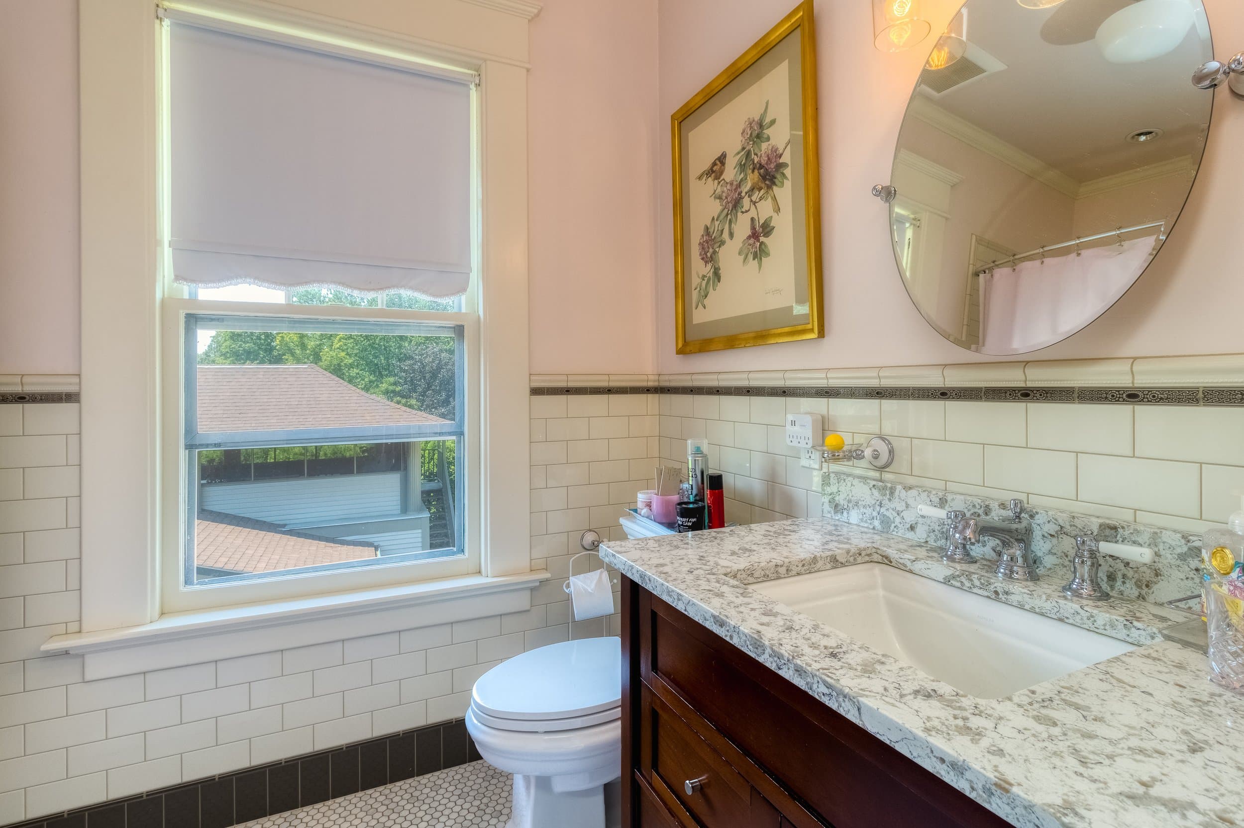 Bright bathroom featuring a window, a marble countertop with a sink, and decorative artwork on the wall.