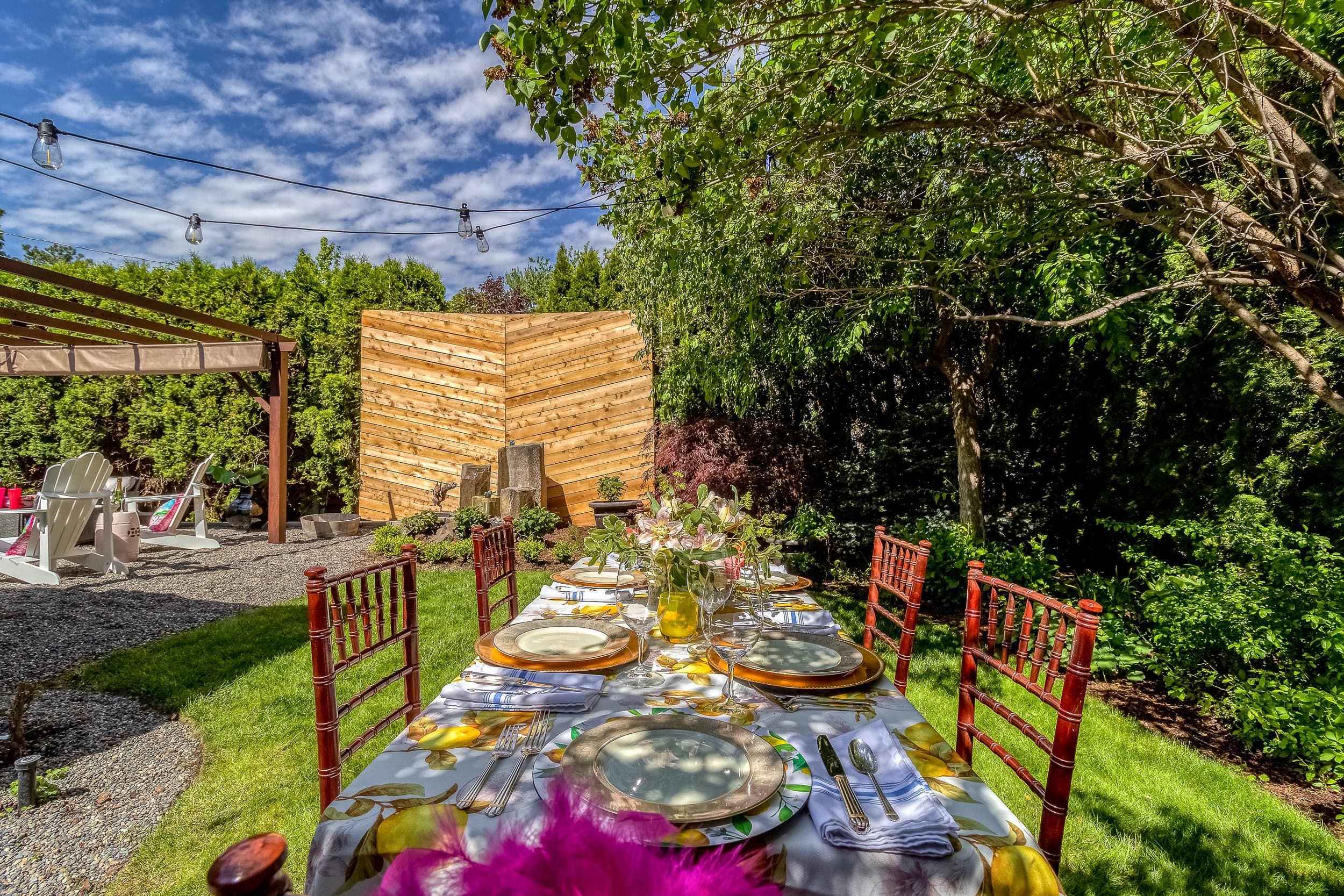 A beautifully set outdoor dining table surrounded by lush greenery and decorative lighting.