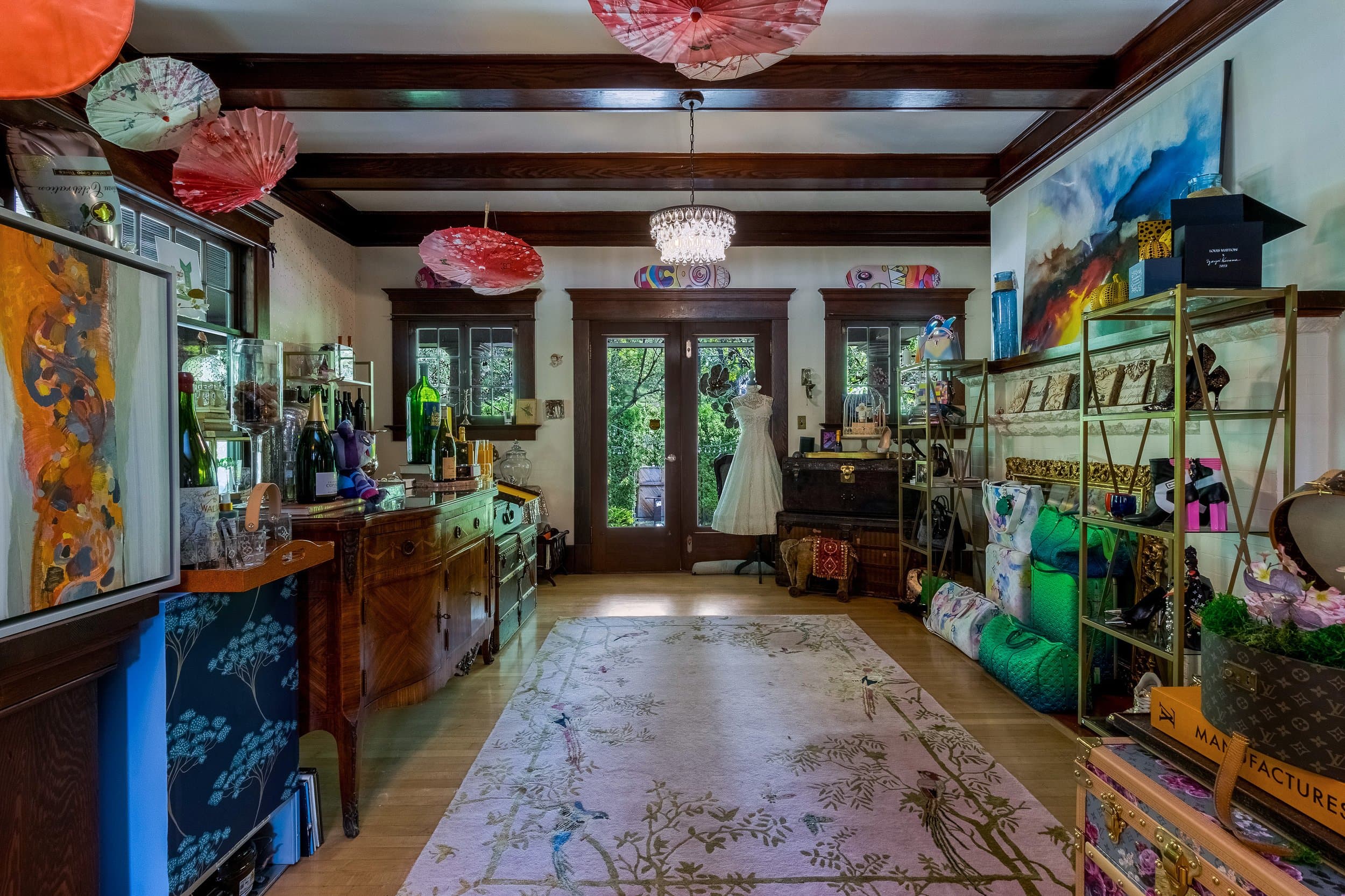 A cozy, eclectic room featuring colorful decor, a vintage wooden sideboard, and lush greenery visible through the doors.