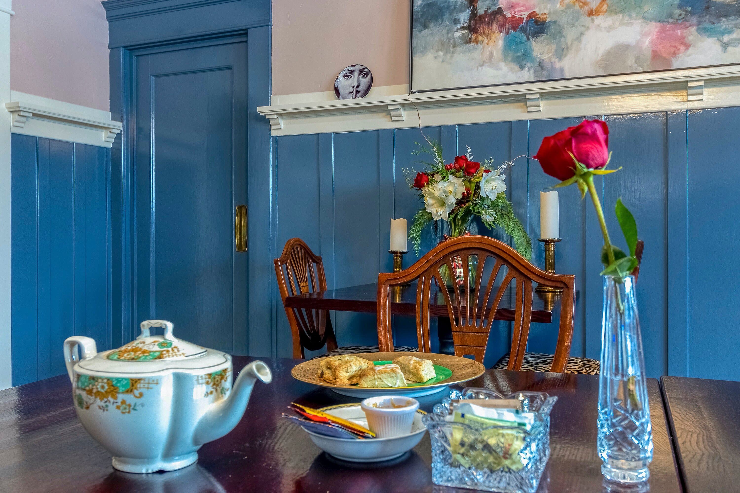 A cozy tea setting featuring a floral arrangement, a teapot, and scones on a table.