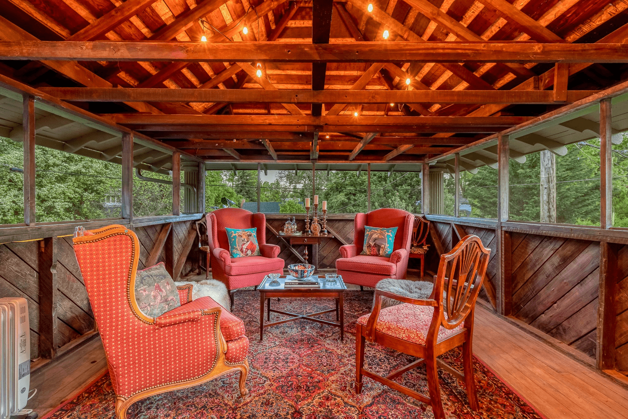 A cozy screened porch featuring two red upholstered chairs, a wooden table, and warm lighting.