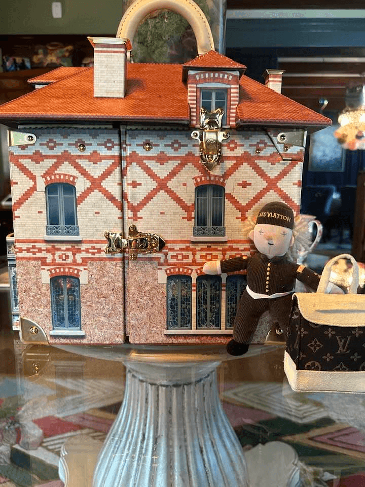 A decorative toy house featuring a teddy bear in a uniform and a small handbag.
