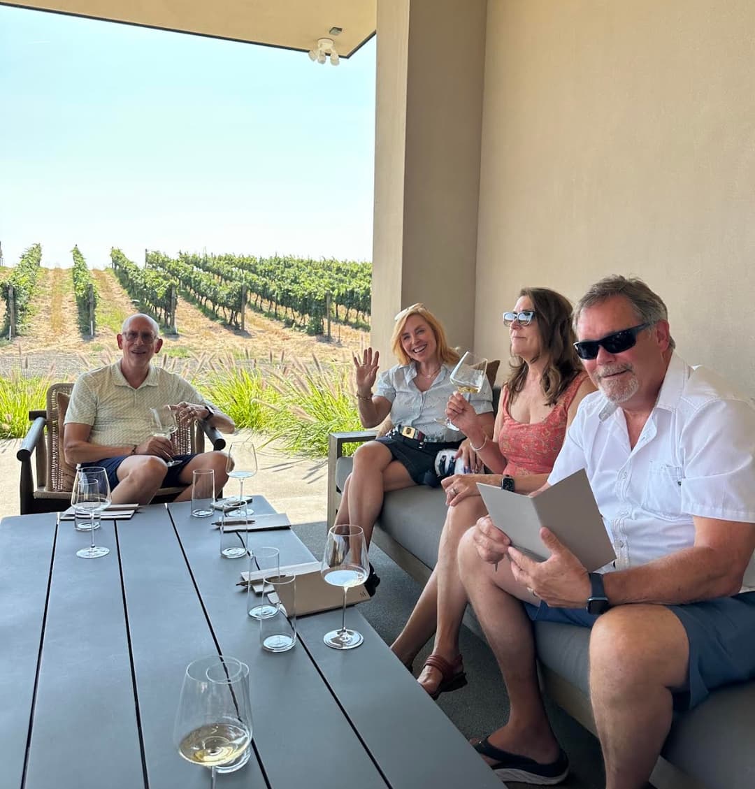 Guests relaxing on a shaded patio with wine glasses in hand, overlooking vineyard rows in Walla Walla during a curated retreat experience.