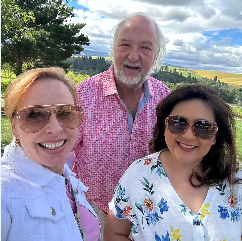 Three smiling guests taking a selfie outdoors in Walla Walla with rolling hills and trees in the background during a retreat experience.